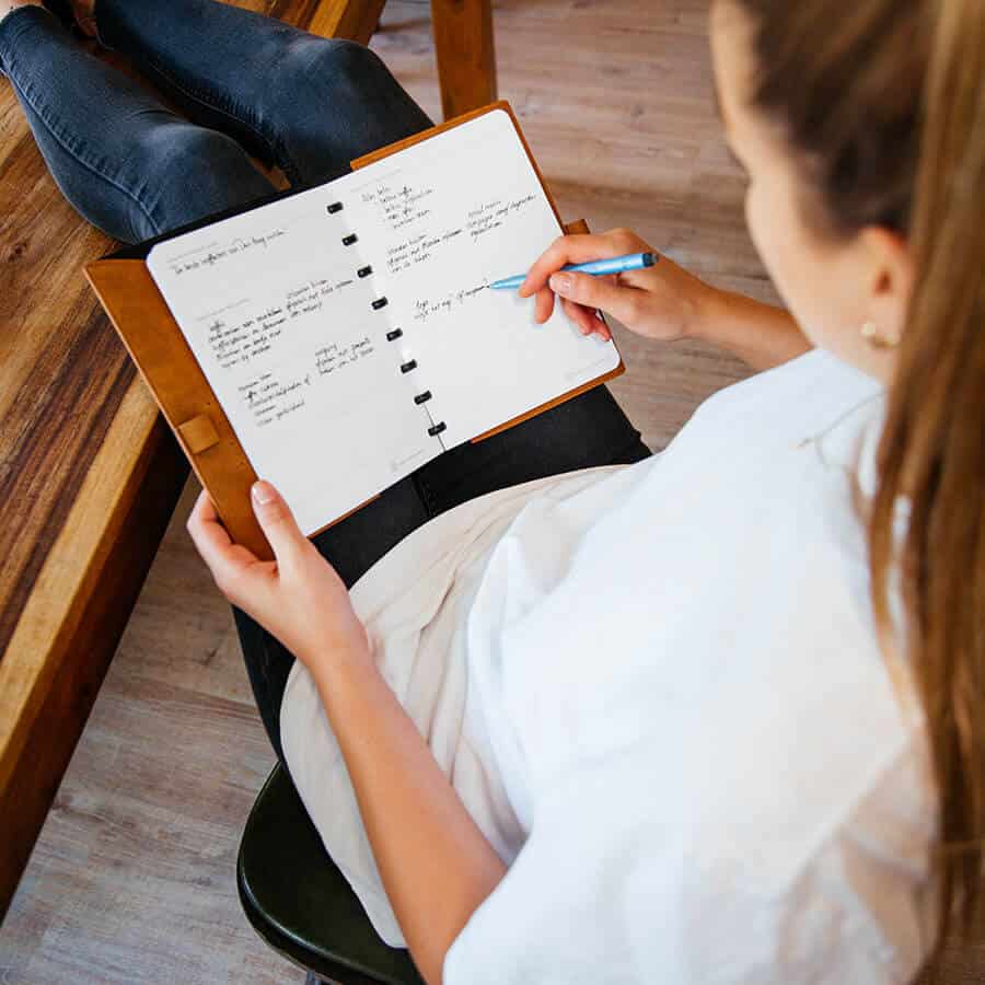 een dame zit met haar benen op tafel en schrijft in een greenbook all in one