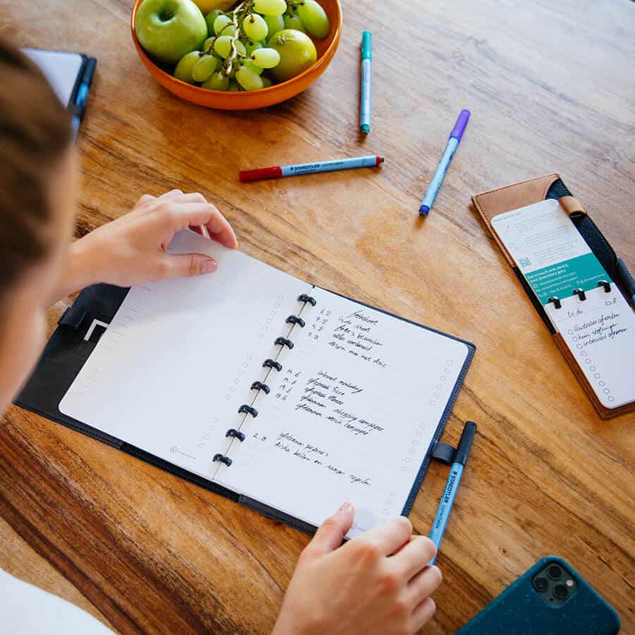 model houdt een to do list boekje vast dat op een keukentafel ligt met accessoires verspreid op de tafel