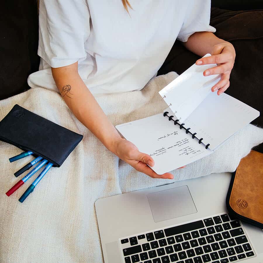 model klikt pagina's in en uit het whiteboard schrift, rechts van haar ligt een etui met pennen en links van haar een cognac werkmap en voor haar een laptop