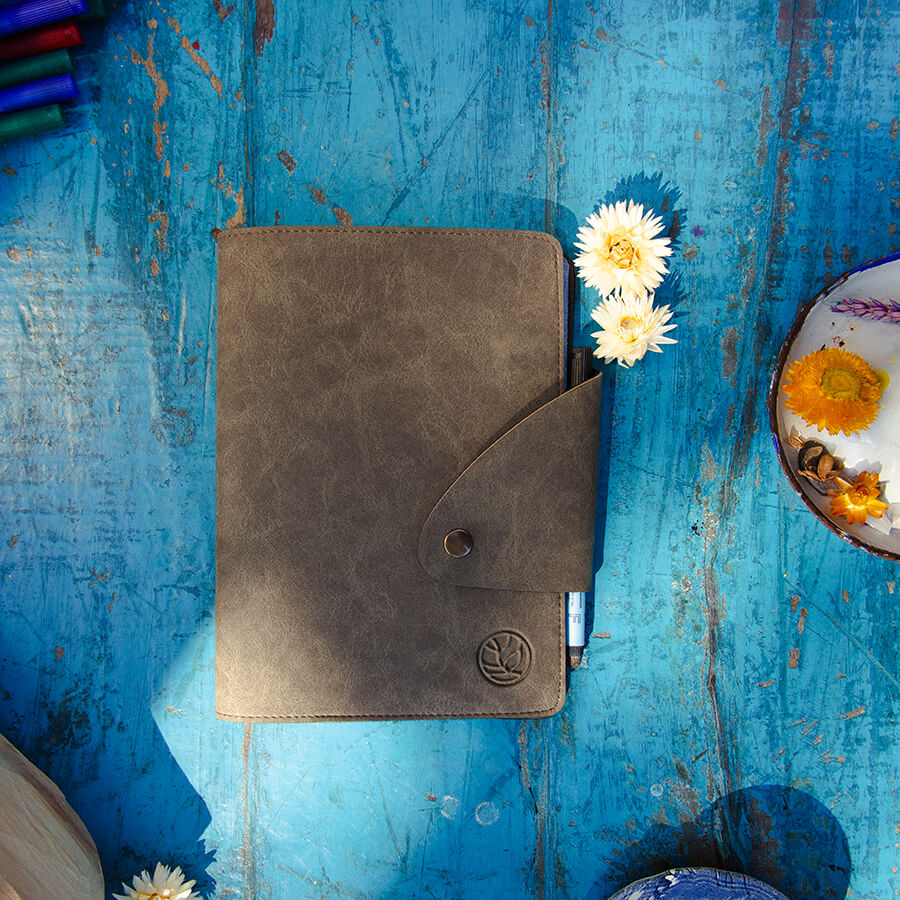 een gesloten whiteboard schrift met een vegan leren omslag in clay kleur, de ondergrond is een blauwe houten tafel